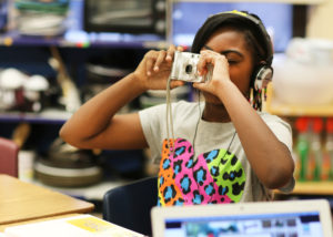 Girl with headphones on is holding a camera up to her face.