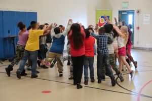 A group of young students in a gymnasium celebrate with raised hands.