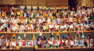 Rows of children hold multicolored ukuleles over their heads.